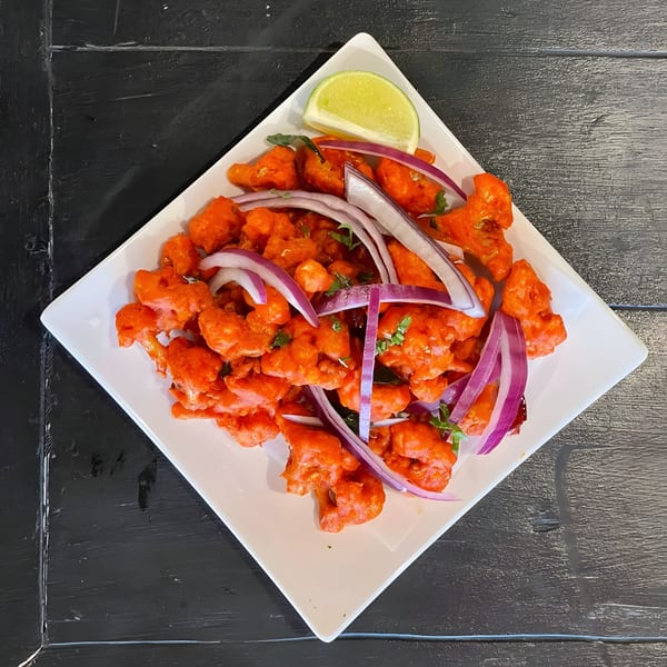 Aaha Indian Cuisine's Gobi Manchurian, featuring crispy cauliflower florets, red onions, and a lime wedge.