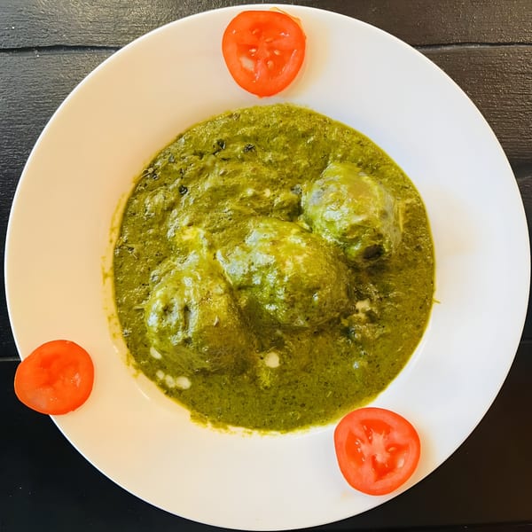 Aaha Indian Cuisine's green spinach curry with paneer cheese and tomato slices on a white plate.