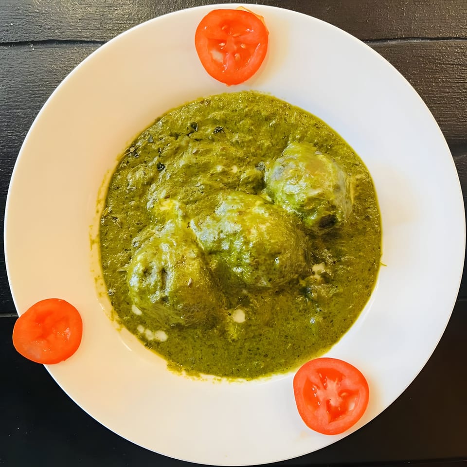Aaha Indian Cuisine's green spinach curry with paneer cheese and tomato slices on a white plate.