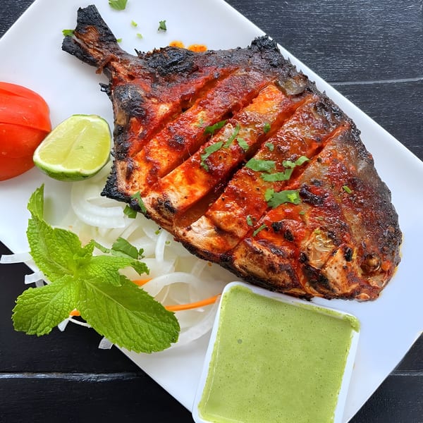Aaha Indian Cuisine's grilled whole fish, garnished with lime, tomato, onions, mint, and green chutney.