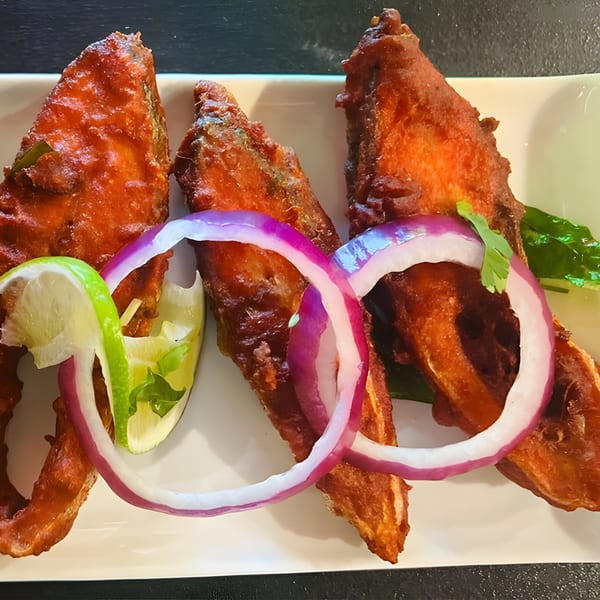 Crispy fried fish pieces, garnished with red onion rings, lime wedges, and cilantro on a white plate.