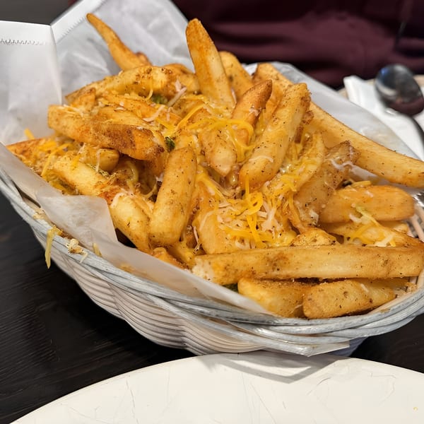 A basket of golden-brown, seasoned french fries topped with melted cheese, served at Aaha Indian Cuisine.