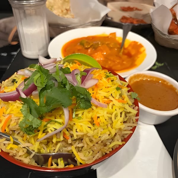 Aaha Indian Cuisine's biryani with red onions, cilantro, and lime, alongside curry and sauce.