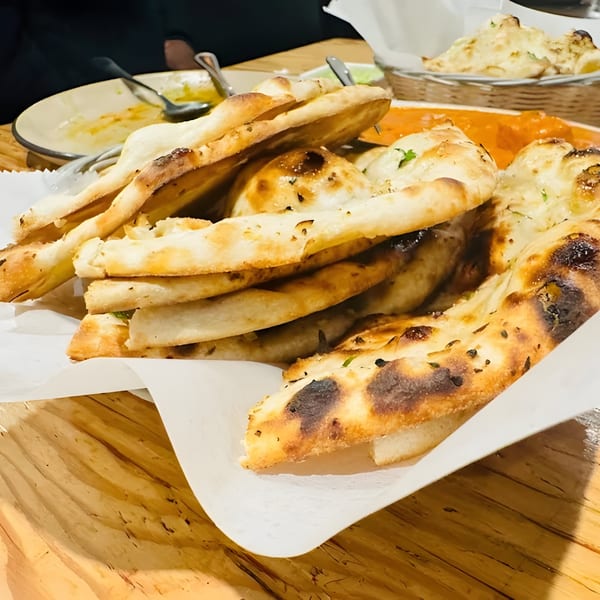 A basket of freshly baked naan bread with a side of orange curry and an empty plate.