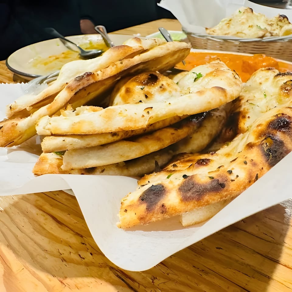 A basket of freshly baked naan bread with a side of orange curry and an empty plate.