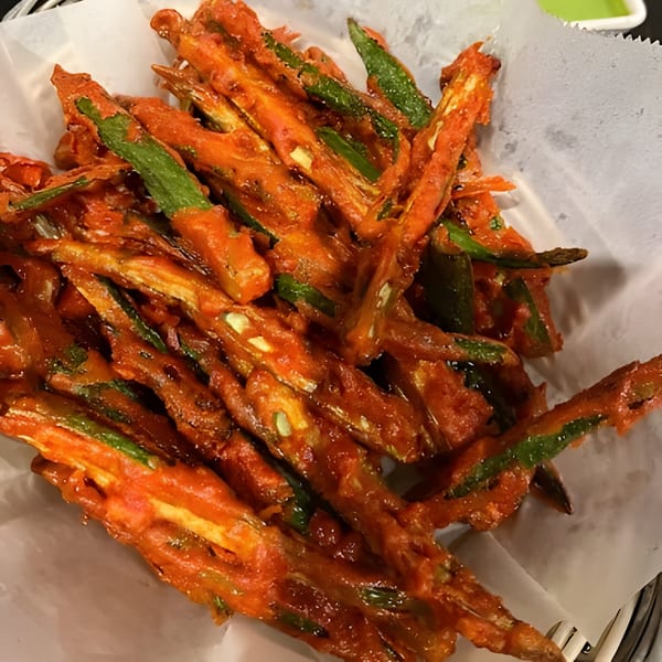 Crispy fried okra, coated in a vibrant orange batter, served in a white paper-lined basket.