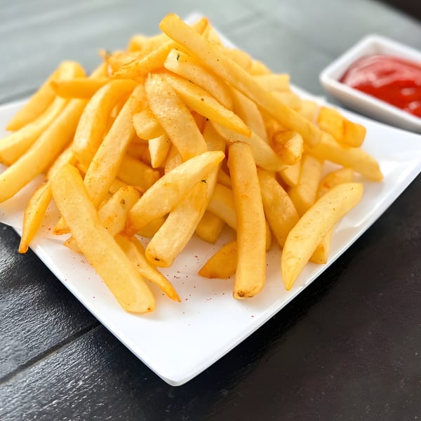 A white rectangular plate piled high with golden french fries, seasoned with spices, and a side of ketchup.