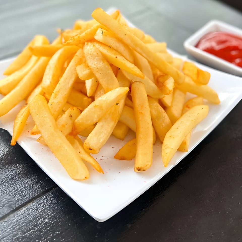 A white rectangular plate piled high with golden french fries, seasoned with spices, and a side of ketchup.
